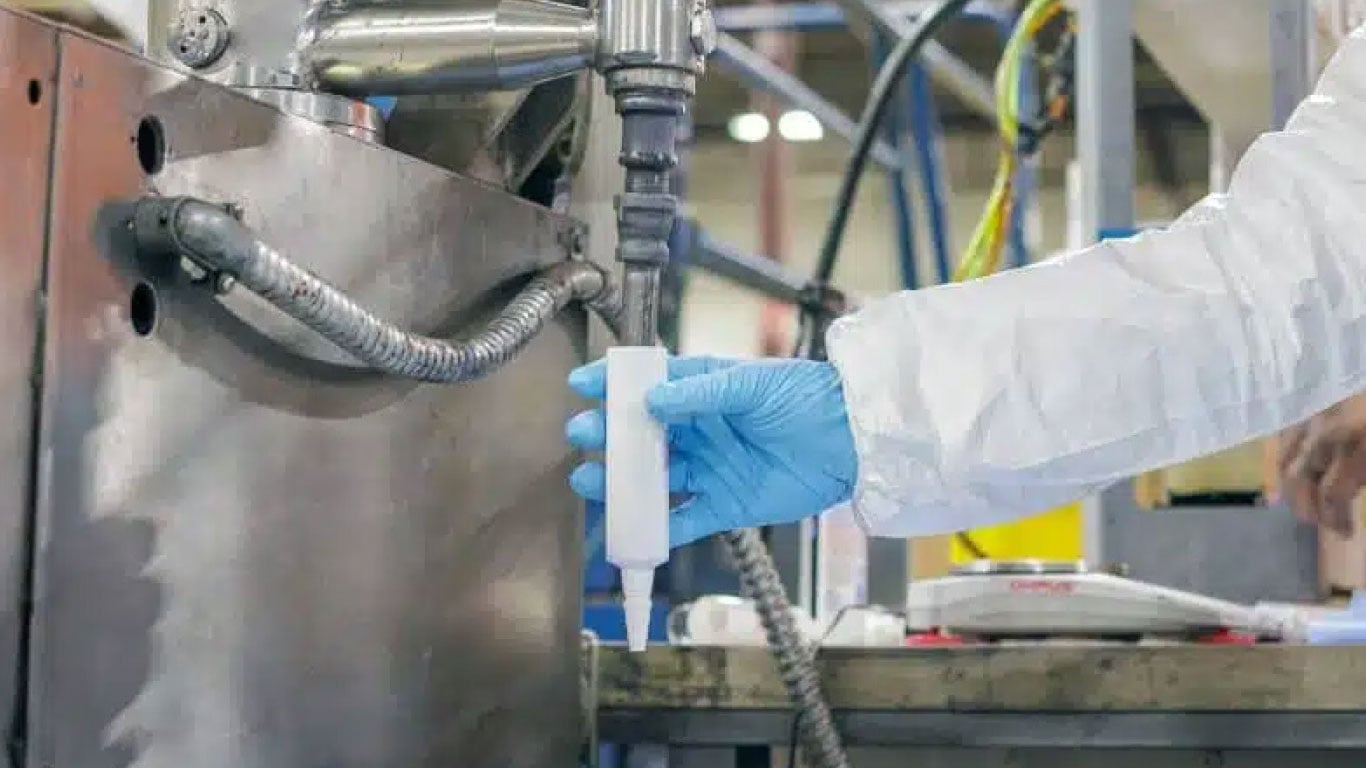 Gloved technician dispensing material with a pneumatic applicator during an industrial manufacturing process.