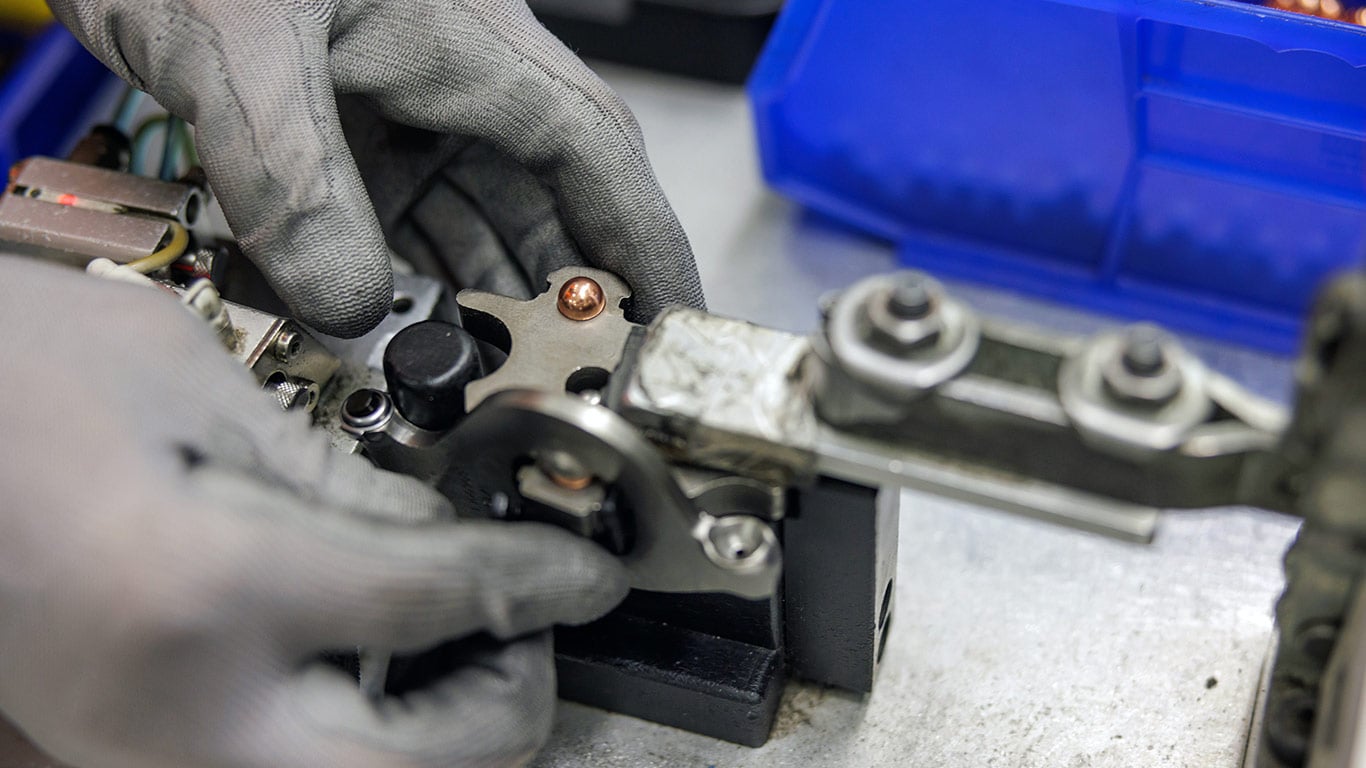 Technician using a handheld power tool to assemble a precision mechanical component on a manufacturing workbench.